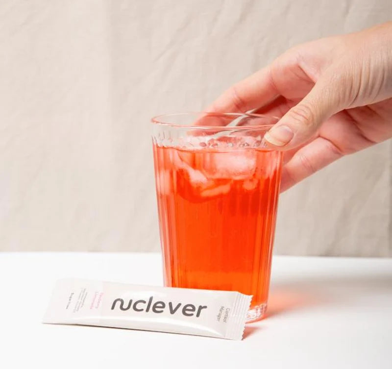 Nutritional supplement packet with pink drink and mixer, alongside a gift box.