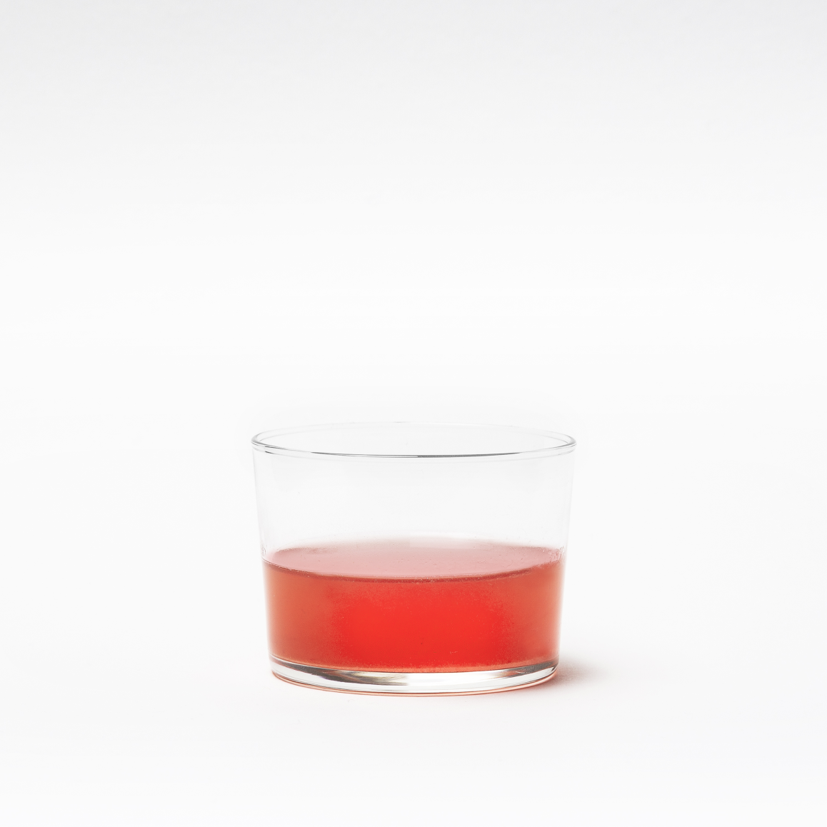 A clear glass with a small amount of red liquid.