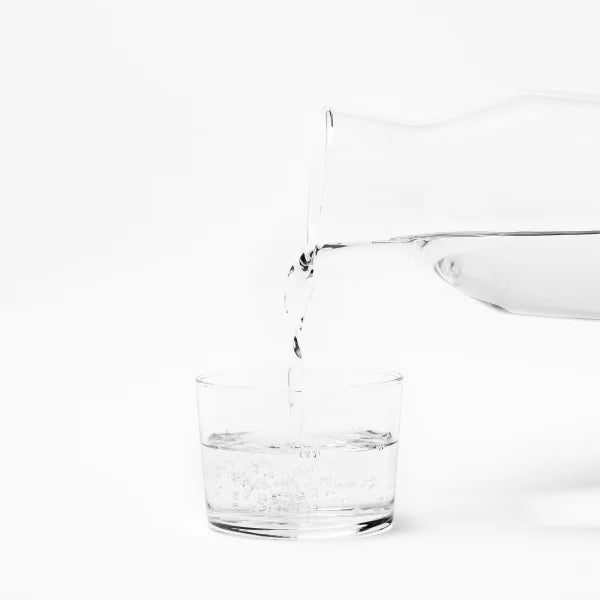 Pouring water from a glass pitcher into a glass on a white background.