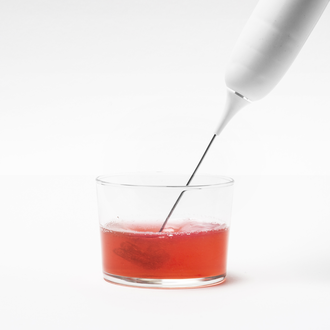 Electric frother in a glass of red liquid on white background.